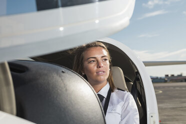 Thoughtful female pilot sitting in airplane against sky at airport - CAVF62031