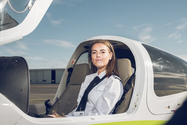 Porträt einer selbstbewussten Pilotin, die in einem Flugzeug gegen den blauen Himmel am Flughafen sitzt - CAVF62034