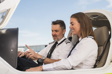 Männlicher Pilot unterrichtet weibliche Auszubildende im Flugzeug vor blauem Himmel am Flughafen - CAVF62036