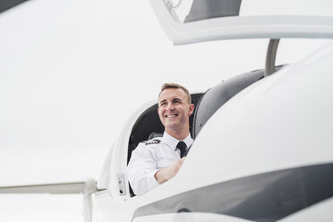 Low angle view of smiling male pilot sitting in airplane against sky at airport - CAVF62037