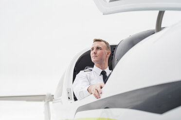 Low angle view of thoughtful male pilot sitting in airplane against sky at airport - CAVF62038