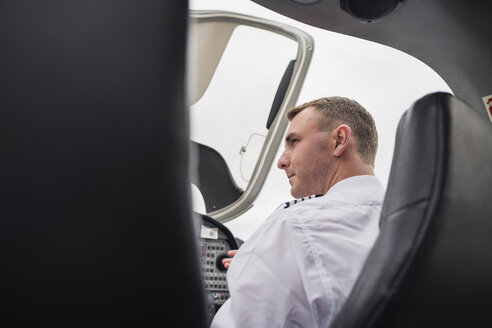 Rückansicht eines ernsthaften männlichen Piloten, der im Flugzeug sitzend gegen den Himmel auf dem Flughafen schaut - CAVF62039