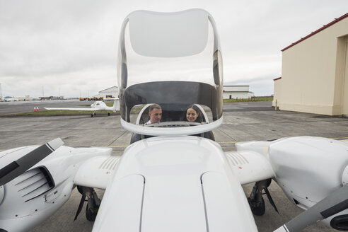 Hoher Blickwinkel des männlichen Piloten, der die weibliche Auszubildende führt, während er im Flugzeug gegen den bewölkten Himmel auf der Startbahn des Flughafens sitzt - CAVF62041