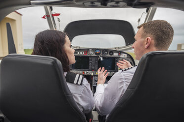 Rear view of male pilot giving training to female trainee while sitting in airplane at airport - CAVF62042