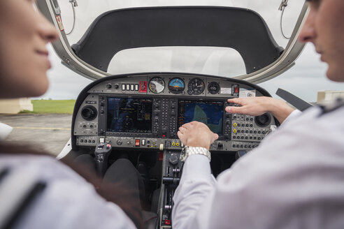 Ausgeschnittenes Bild eines männlichen Piloten, der einer weiblichen Auszubildenden das Armaturenbrett zeigt, während er im Flugzeug am Flughafen sitzt - CAVF62043