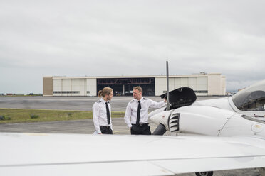 Ein Ingenieur zeigt einem männlichen Auszubildenden Flugzeugteile, während er auf der Startbahn eines Flughafens vor einem bewölkten Himmel steht - CAVF62044