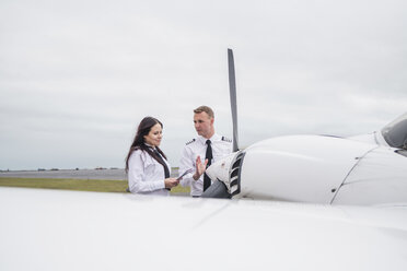 Ingenieur zeigt weiblicher Auszubildender Flugzeugteile, während er auf der Start- und Landebahn eines Flughafens vor bewölktem Himmel steht - CAVF62045