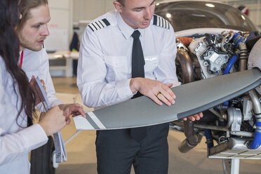 Ingenieur zeigt Auszubildenden die Tragfläche eines Flugzeugs, während er im Hangar steht - CAVF62049