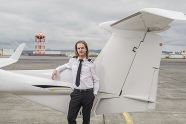 Porträt eines zuversichtlichen männlichen Piloten, der neben einem Flugzeug auf der Startbahn eines Flughafens steht, bei bewölktem Himmel - CAVF62051