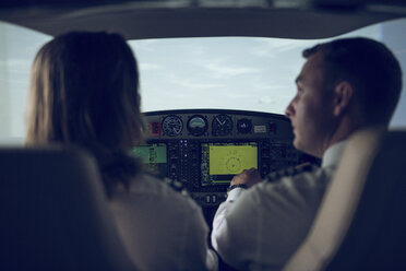 Rear view of pilot giving training to male trainee in flight simulator - CAVF62059