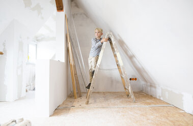 Boy standing on ladder in attic to be renovated - MFRF01167