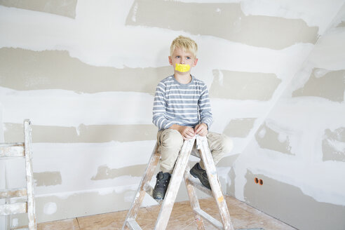 Wütender Junge mit zugeklebtem Mund sitzt auf einer Leiter in einem zu renovierenden Dachboden - MFRF01193