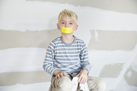 Porträt eines Jungen mit zugeklebtem Mund, der auf einer Leiter auf einem zu renovierenden Dachboden sitzt, lizenzfreies Stockfoto