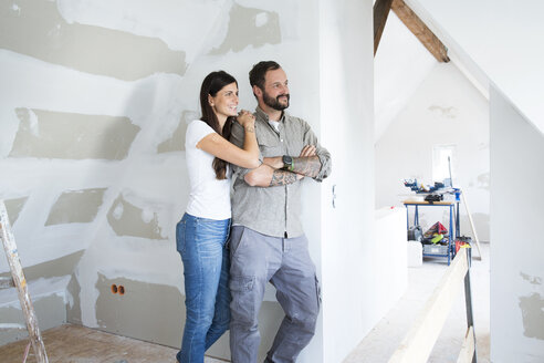 Smiling couple in attic to be renovated looking out of window - MFRF01195