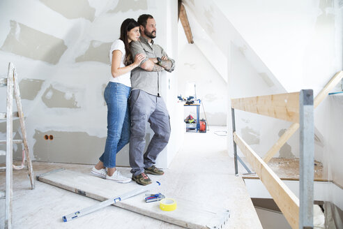 Ehepaar im zu renovierenden Dachgeschoss schaut aus dem Fenster - MFRF01196