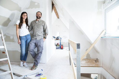 Portrait of confident couple standing in attic to be renovated - MFRF01199