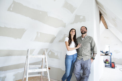 Confident couple standing in attic to be renovated looking up - MFRF01200