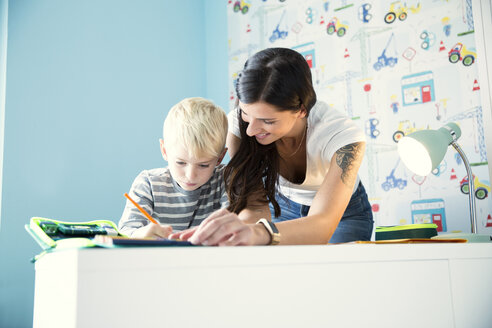 Mutter hilft Sohn bei den Hausaufgaben am Schreibtisch - MFRF01209