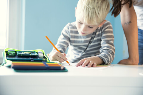 Junge bei den Hausaufgaben, Mutter stützt sich auf den Schreibtisch, lizenzfreies Stockfoto