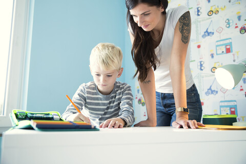 Mutter hilft Sohn bei den Hausaufgaben am Schreibtisch, lizenzfreies Stockfoto