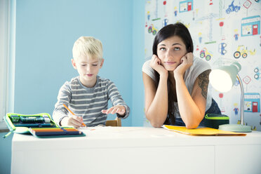 Portrait of pensive mother with son doing homework at desk - MFRF01213