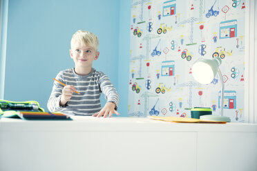 Smiling boy doing homework at desk in children's room - MFRF01215