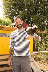 Portrait of smiling man with Polish chicken at chickenhouse in garden - MFRF01231
