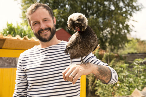 Portrait of smiling man with Polish chicken at chickenhouse in garden - MFRF01232