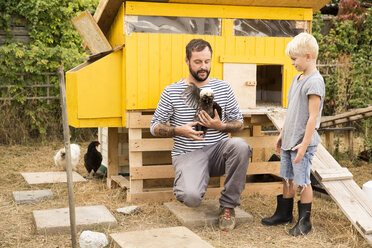 Vater und Sohn mit polnischen Hühnern im Hühnerstall im Garten - MFRF01244