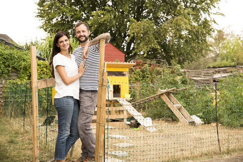Portrait of confident couple standing at chickenhouse in garden - MFRF01266