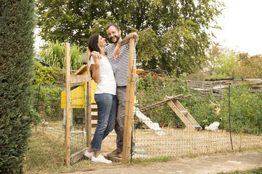Happy couple standing at chickenhouse in garden - MFRF01268