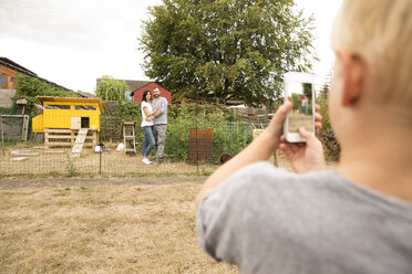 Junge macht Handy-Foto von Eltern im Hühnerstall im Garten - MFRF01270