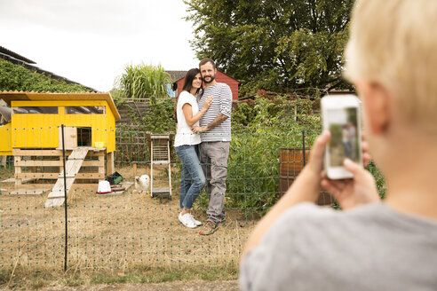 Junge macht Handy-Foto von Eltern im Hühnerstall im Garten - MFRF01271