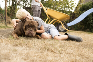Junge kuschelt mit alter englischer Bulldogge auf Spielplatz im Garten - MFRF01273