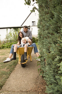 Playful man pushing wife and son sitting in wheelbarrow in garden - MFRF01278