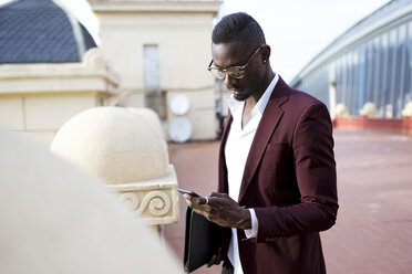 Young entrepüreneur wating on hotel terrace for his appointment, using smartphone - JSRF00145