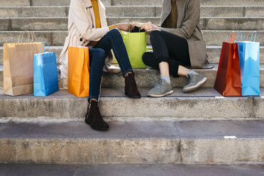 Two women with shopping bags sitting on stairs checking the purchase - JRFF02770