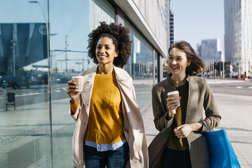 Zwei glückliche Frauen mit Einkaufstaschen und Kaffee zum Mitnehmen beim Spaziergang in der Stadt - JRFF02773