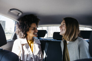 Zwei glückliche Frauen sitzen auf dem Rücksitz eines Autos - JRFF02801