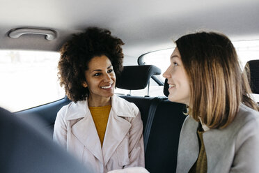 Zwei glückliche Frauen sitzen auf dem Rücksitz eines Autos - JRFF02802