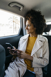 Smiling woman sitting in back seat of a car holding cell phone - JRFF02803