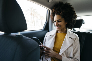 Lächelnde Frau auf dem Rücksitz eines Autos, die ein Mobiltelefon benutzt - JRFF02804
