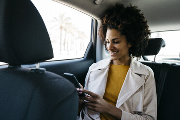 Smiling woman sitting in back seat of a car using cell phone - JRFF02804