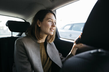 Lächelnde Frau, die auf dem Rücksitz eines Autos sitzt und ein Mobiltelefon hält - JRFF02805