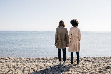 Rückenansicht von zwei Freunden, die am Strand stehen und auf das Meer schauen - JRFF02809