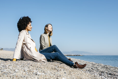 Zwei Freunde sitzen am Strand und genießen ihre Freizeit, lizenzfreies Stockfoto