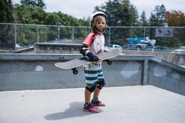Porträt eines Mädchens, das ein Skateboard hält und auf einer Sportrampe im Park steht - CAVF62119