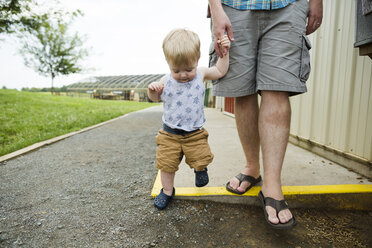 Tiefschnitt eines Vaters, der die Hände seines Sohnes hält, während er auf dem Fußweg auf dem Markt spazieren geht - CAVF62126