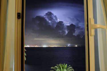 Blick auf Gewitterwolken über dem Meer durch ein Fenster bei Nacht - CAVF62127