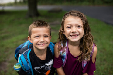 Portrait of smiling siblings with backpack standing on field - CAVF62138